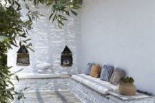 a Mediterranean terrace with white stone and plaster wlals, niches for storage, printed throws and candle lanterns