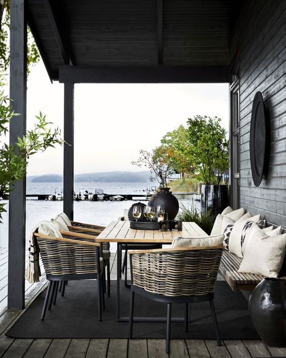 a Nordic space with wicker chairs, a wooden table and bench, lots of greenery in pots and blakc tableware