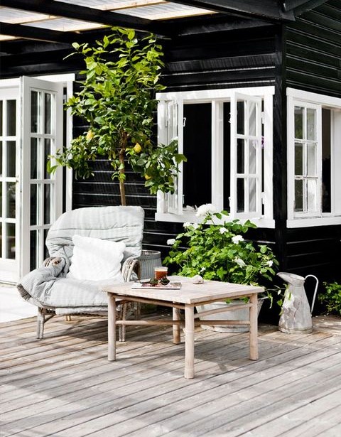 a Nordic terrace with natural wooden furniture, potted greenery and a tree, rattan chairs
