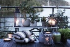 a Nordic terrace with pots and planters with greenery, succulents, candle lanterns and striped pillows