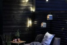 a Scandinavian terrace with birdhouse lights, potted greenery, lots of candles and crate and wooden furniture