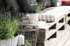 a Scandinavian terrace with crate furniture, printed pillows, potted greenery and blooms, a cage with candles and greenery