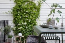 a Scandinavian terrace with dark green metal furniture, climbing greenery and blooms, potted plants and a rattan chair