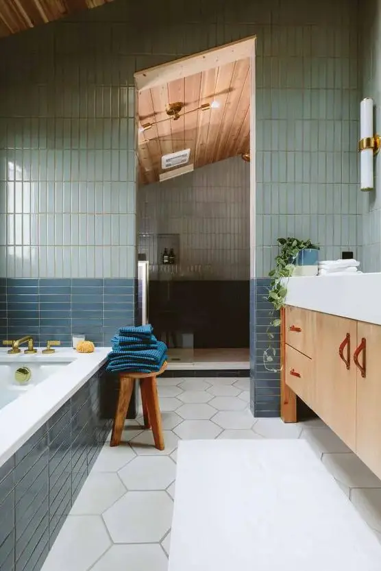 a bathroom with pale blue and navy skinny tiles and white hexagon ones, with a large shower space and a tub clad with tiles