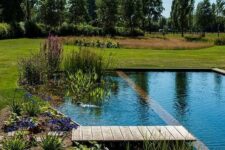 a beautiful swimming pond with a brick border and a wooden deck, plants and blooms around is super chic