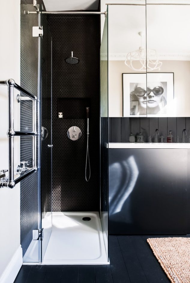 a black and white bathroom with a shower done with black penny tiles, a black wall with a storage shelf and some art
