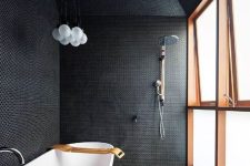 a black bathroom fully clad with penny tiles with white grout, with a frosted glass wall and a free-standing bathtub