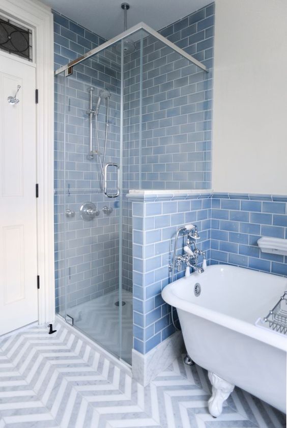 a blue bathroom with blue subway tiles, a chevron floor, a white bathtub and a shower zone