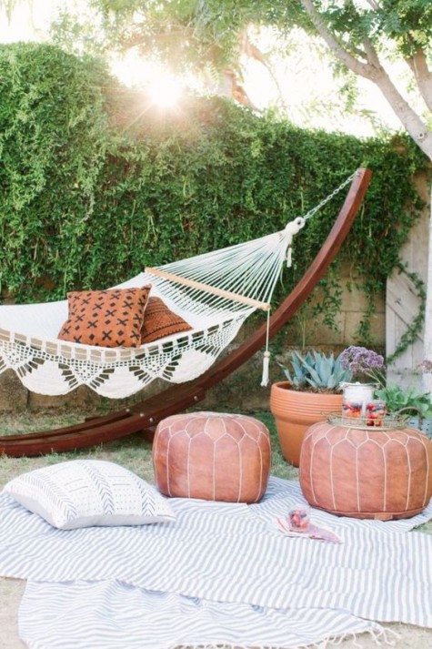 a boho Moroccan patio with striped blankets, leather ottomans and a macrame hammock with printed pillows