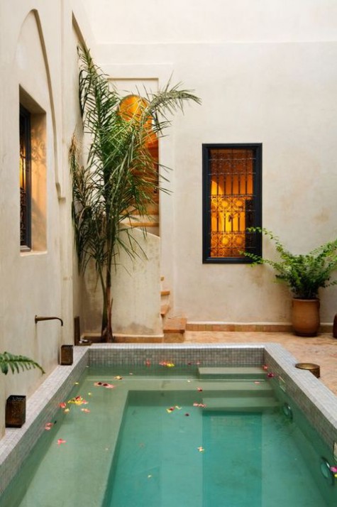 a boho Moroccan space with a plunge pool with benches inside, some tropical trees in planters and greenery