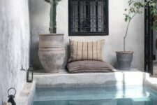 a boho chic backyard done in concrete and plaster, with a plunge pool, pillows, potted cacti and lanterns