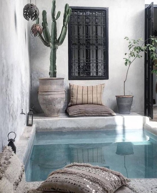 a boho chic backyard done in concrete and plaster, with a plunge pool, pillows, potted cacti and lanterns