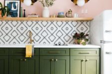 a bold boho kitchen with a pink wall, geometric tiles, a boho rug, green cabinets and gold touches
