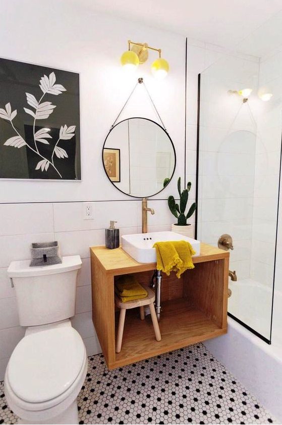 a bold mid-century modern bathroom with black and white penny tiles on the floor, a floating vanity, a round mirror and yellow touches
