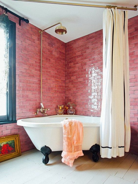 a bold pink bathroom clad with subway tiles, a clawfoot tub, a large curtain, gold touches and refined decor