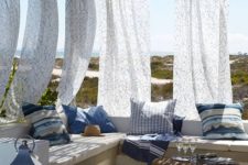 a breezy Mediterranean terrace with a concrete bench with printed pillows, candle lanterns, a rattan table and printed curtains