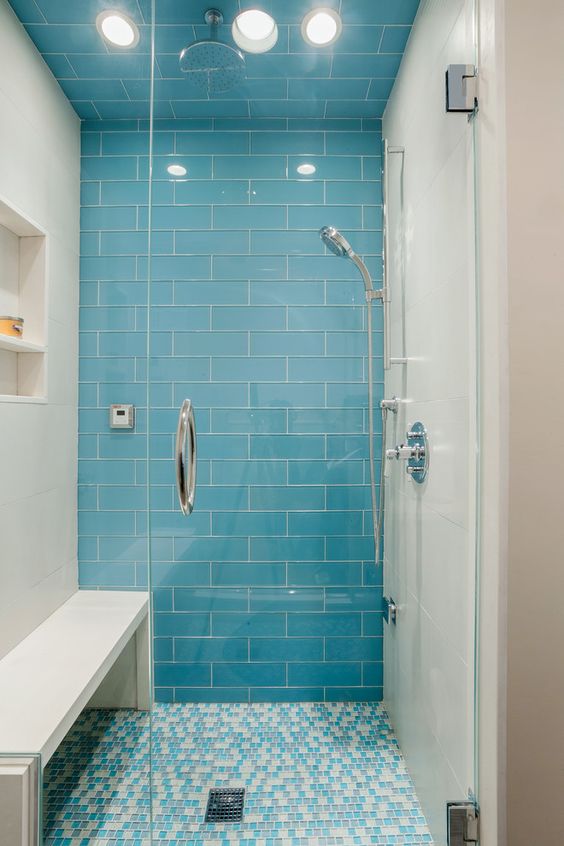 a bright bathing space with blue subway and small mosaic tiles, with a niche shelf and a bench