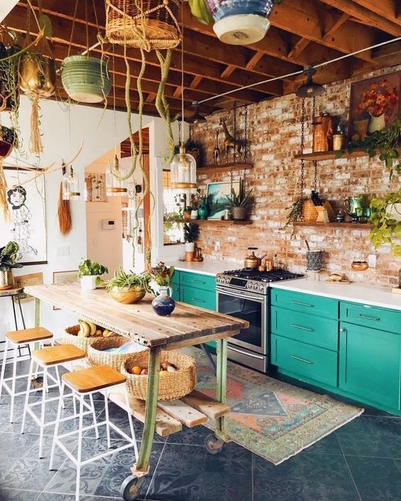 a bright boho kitchen with turquoise cabinets, a boho rug, a wooden kitchen island, a brick wall and suspended pots