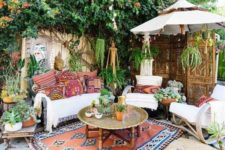 a bright boho terrace with colorful printed textiles, potted greenery, a metal table and carved wooden furniture