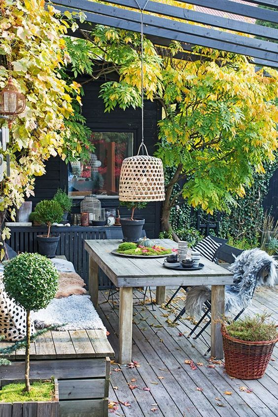 a chic Nordic terrace with weathered wood furniture, a lamp hanging over the table, potted greenery, moss and black items
