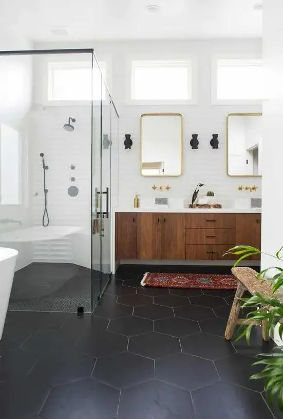 a chic mid-century modern bathroom with black hex tiles on the floor, a boho rug, a wooden floating vanity and touches of gold