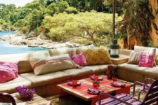 a colorful Mediterranean terrace with bright pink chairs, thrwos, bold textiles and candle lanterns plus a sea view