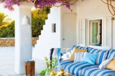 a colorful Mediterranean terrace with bright striped furniture, bright blooms over the terrace, a vintage table and a jute rug