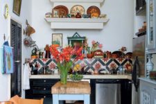 a colorful boho kitchen with bright tiles on the floor and backsplash, a blue table, colorful plates on the shelves and bright furniture