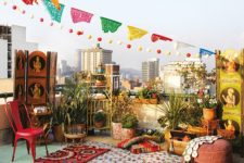 a colorful boho rooftop terrace with colorful banners and garlands, potted greenery and blooms, a striped mattress and printed textiles