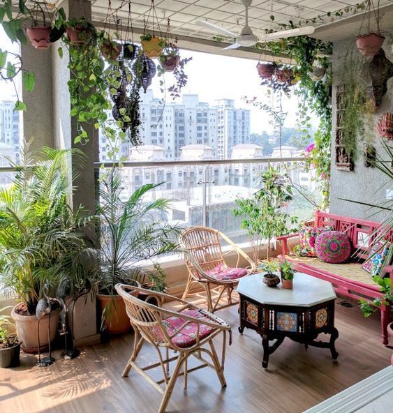 a colorful boho terrace with rattan chairs, a pink bench, potted greenery hanging and a heavy dark carved table