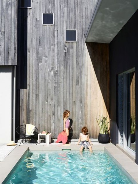 a contemporary backyard with a plunge pool, a wooden deck, some furniture and greenery in pots