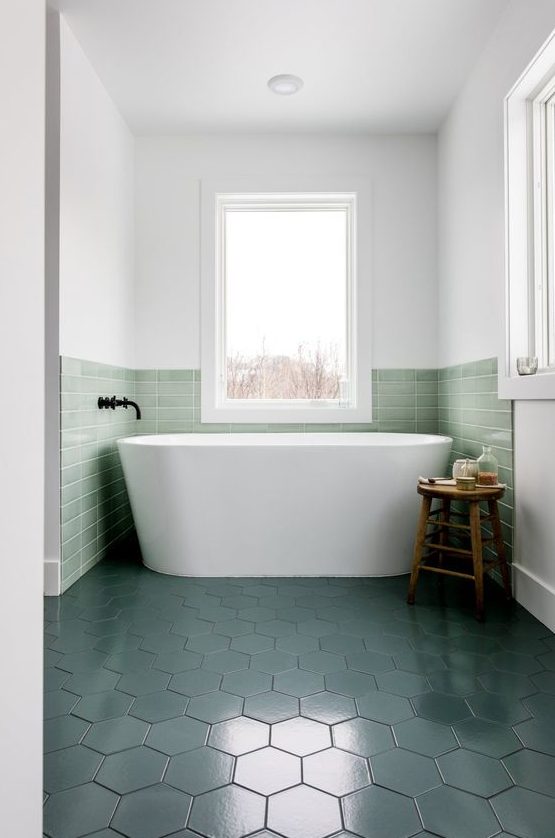 a contemporary bathroom with a bathtub niche covered with green tiles that match dark green floors
