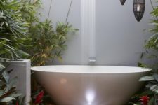 a contemporary bathroom with an oval tub, growing greenery, candles and a waterfall shower