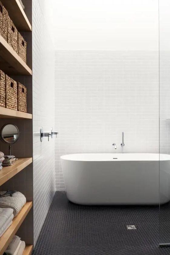 a contemporary bathroom with white stacked tiles and black penny ones, an oval tub, a wooden storage unit