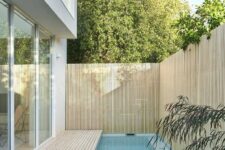 a contemporary outdoor space with a wooden deck and a small and narrow pool plus a wood slat fence around