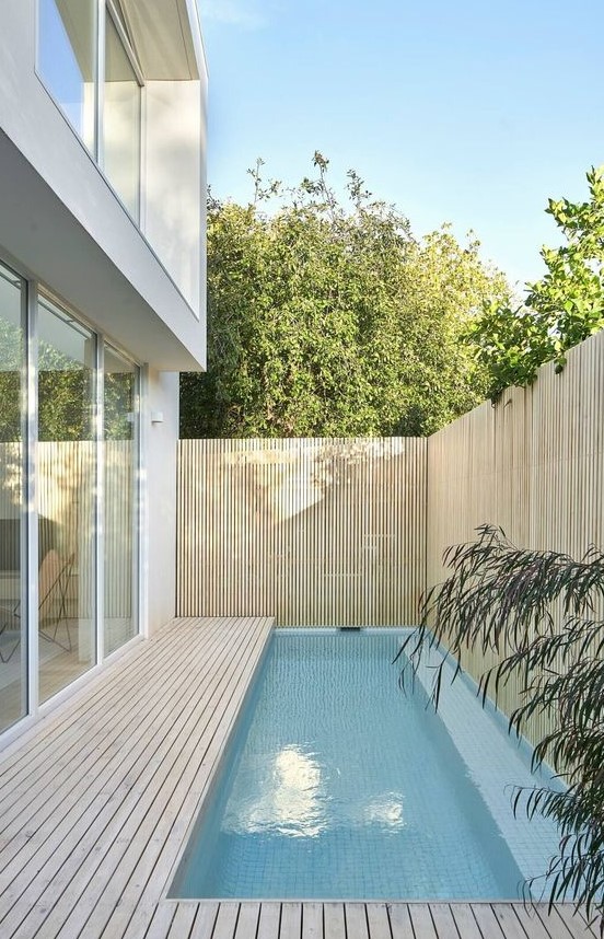 a contemporary outdoor space with a wooden deck and a small and narrow pool plus a wood slat fence around