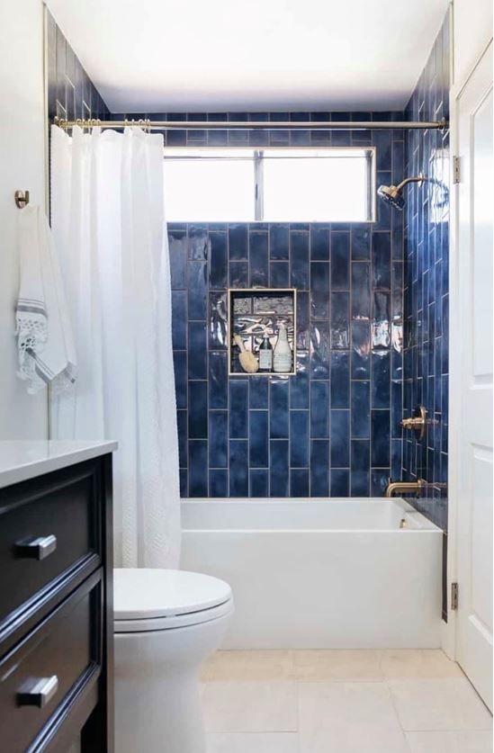 a contrasting bathroom with bold navy subway tiles in the bathing space, a tub, a dark vanity and white textiles