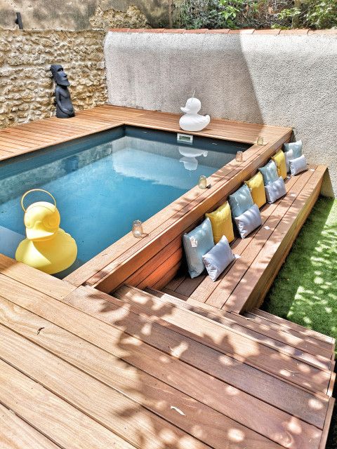 a cozy backyard with a pool and a raised wooden deck, some pillows and fun duck decor is an ultimate space to refresh yourself