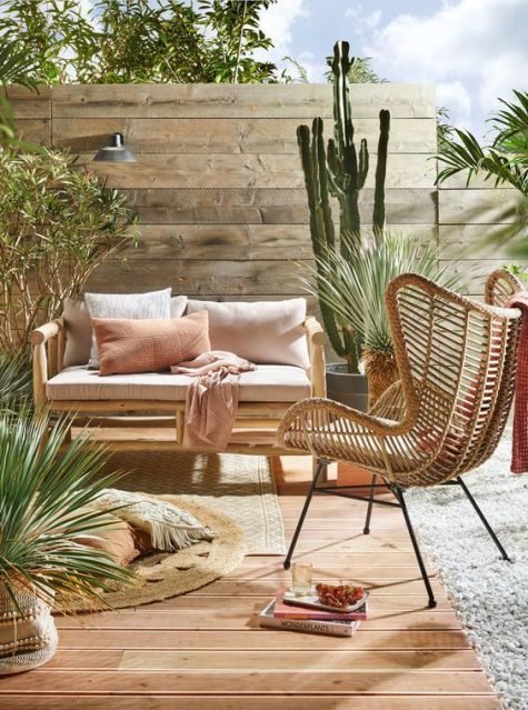 a cozy neutral boho desert terrace with a rattan chair, a wooden sofa, jute rugs, cacti and greenery