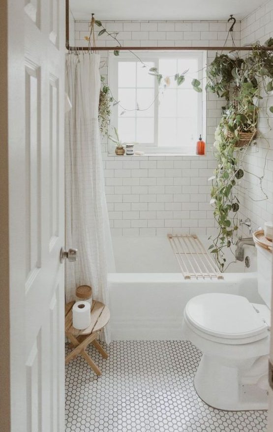 a cozy tiny bathroom clad with marble hex tiles and white subway ones, potted greenery and a wooden stool is a stylish and welcoming space