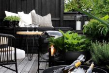 a dark Nordic terrace with blakc walls, planters and bowls, metal and wooden furniture, a catchy floor lamp and greenery that refreshes the space