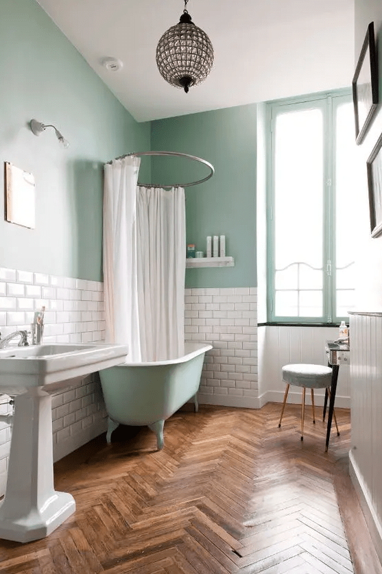 A dreamy aqua colored bathroom with subway tiles used for a backsplash, a free standing sink and a sphere pendant lamp