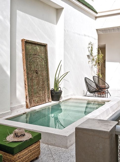 a fantastic Moroccan inspired backyard with a small white pool, a vintage wooden door, wicker and rattan furniture