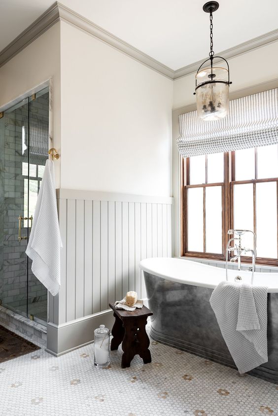 a farmhouse bathroom done with grey paneling, a marble penny tile floor, a grey tub, a shower and vintage lamps