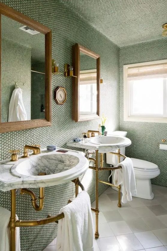 a grene bathroom clad with penny tiles, a neutral floor, free-standing sinks, mirror and gold and brass fixtures