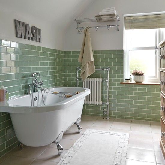 A lovely bathroom done with green subway tiles, a free standing tub, a shower and some decor