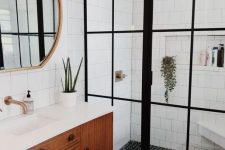 a lovely mid-century modern bathroom with white subway, black and white penny tiles, a stained vanity, a round mirror and a shower
