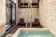 a minimal outdoor space with stone walls, a dark-stained furniture, a plunge pool, some trees and wooden chairs