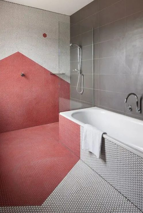 a modern bathroom done with large format stone tiles, red and white penny tiles and a shower and a tub