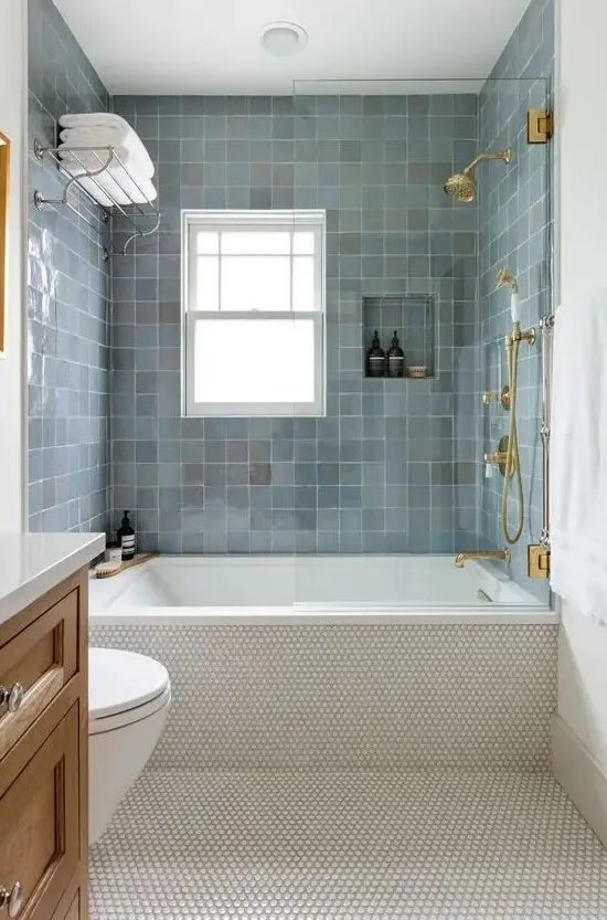 a modern bathroom with penny tiles and blue zellige ones around the tub, a timber vanity, gold and brass fixtures